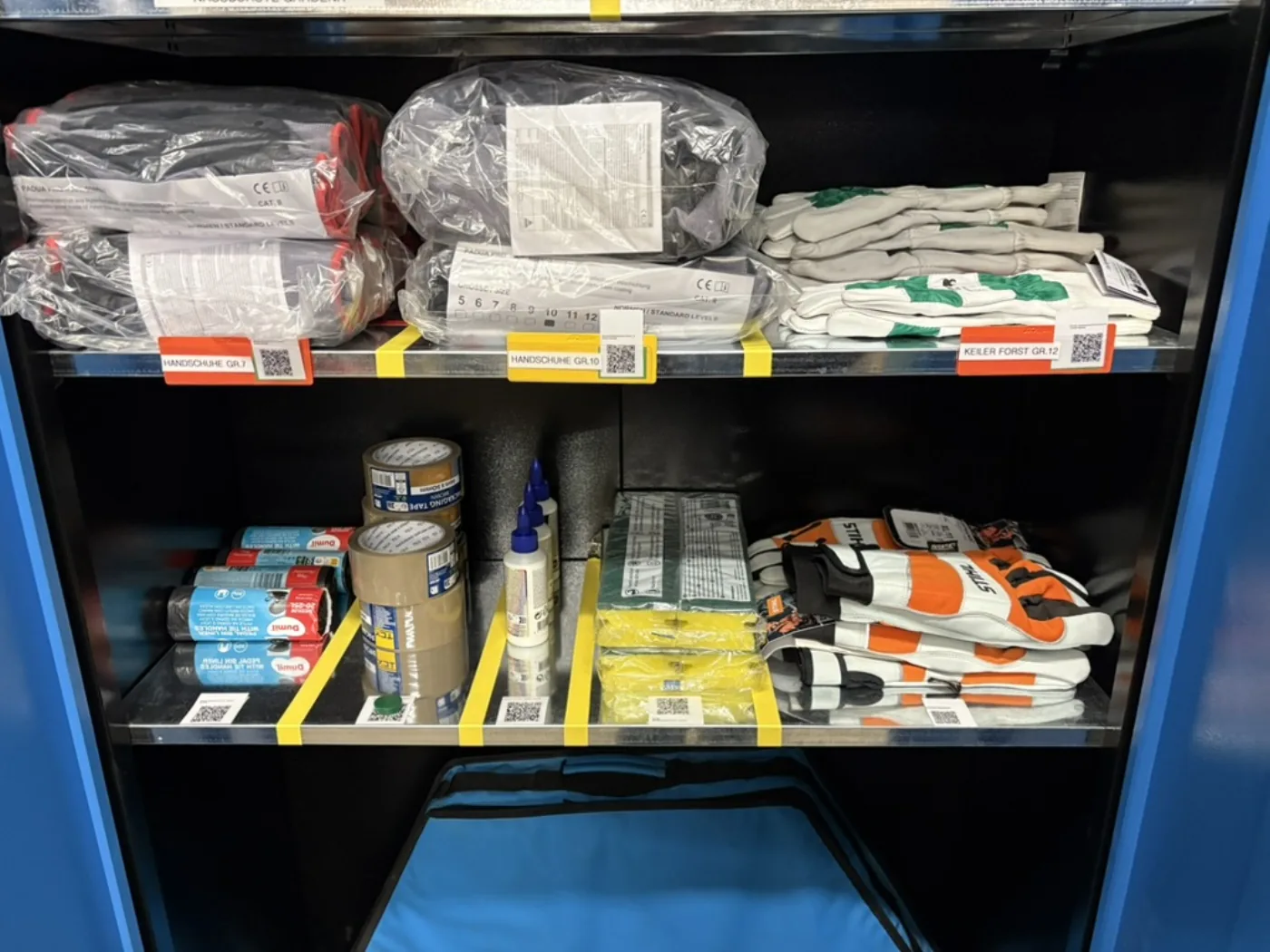Blauer Werkzeugschrank mit Arbeitshandschuhen, Klebeband und Kleber, jedes Fach mit QR-Code-Etikett