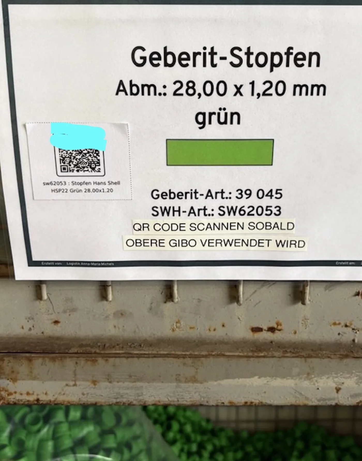 Hinweisschild für Dichtstopfen mit Artikelnummer, Farbmuster und Nachbestell-QR-Code über einer Gitterbox